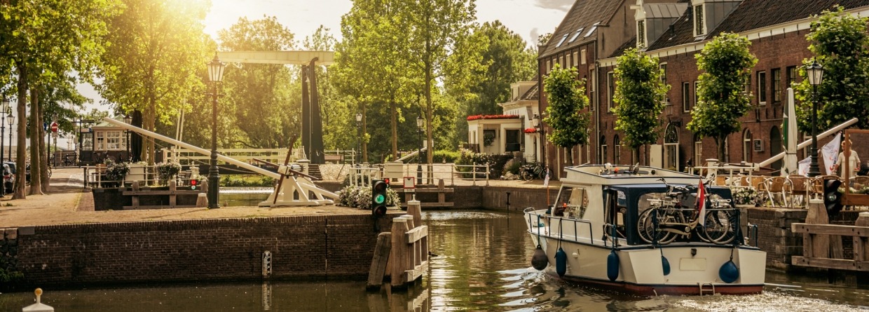 Boot langs een met bomen omzoomde smalle gracht in de zonsopgang bij Weesp. Rustig en gezellig dorp vol grachten en groen vlakbij Amsterdam.